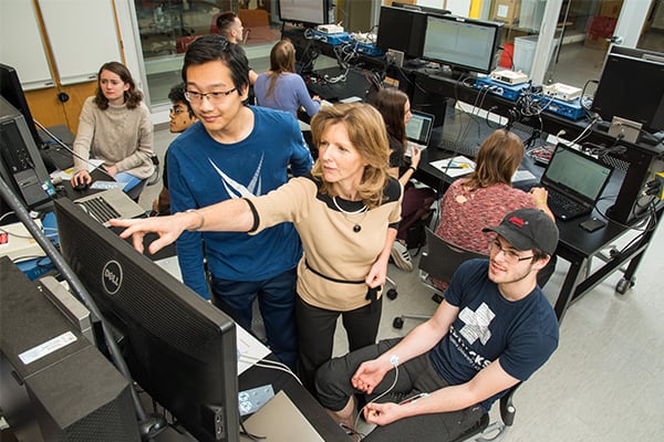 A female professor works with students in the computer lab.