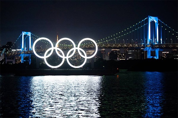 The Olympic rings are lit up in front of a bridge.