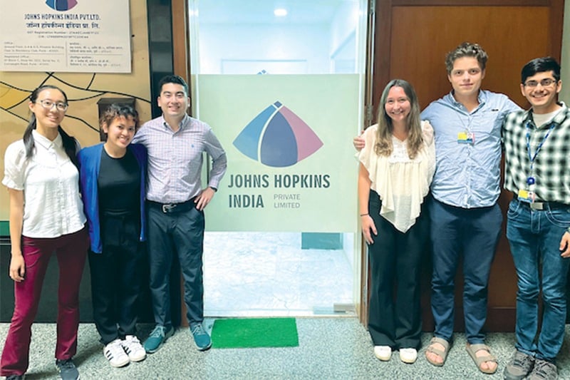 A group of student pose for a photo in front of a Johns Hopkins India sign.